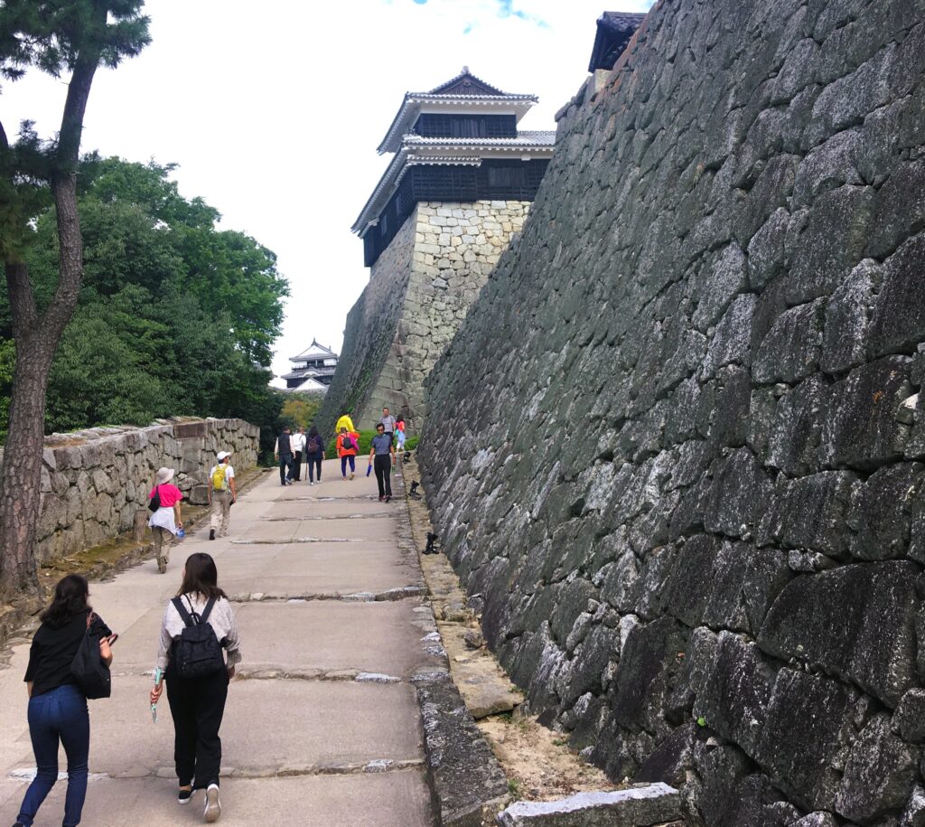 De toegang naar Matsuyama castle, met een aantal toeristen in fleurige kleding die naar boven wandelen.